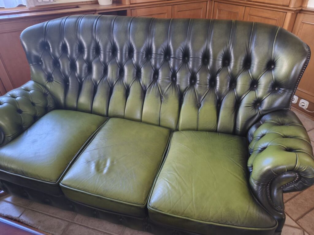 Zöld Chesterfield háromszemélyes bőrkanapé az üléskárpitozás előtt, megnyúlt és kifakult ülőpárnákkal
